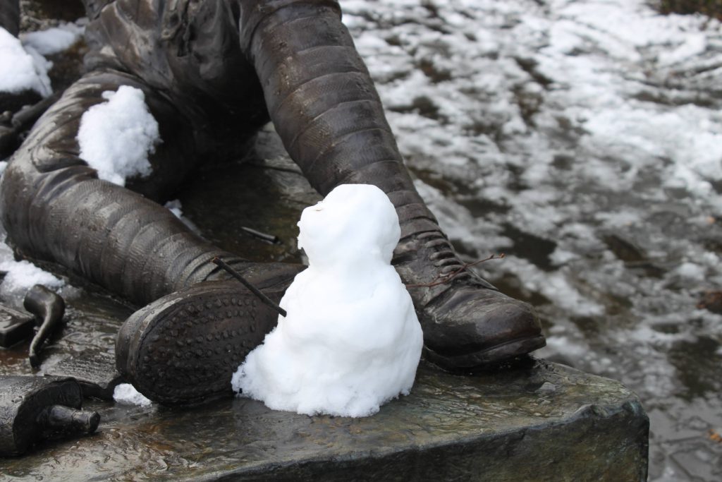 A small snowman at the foot of a statue of a soldier